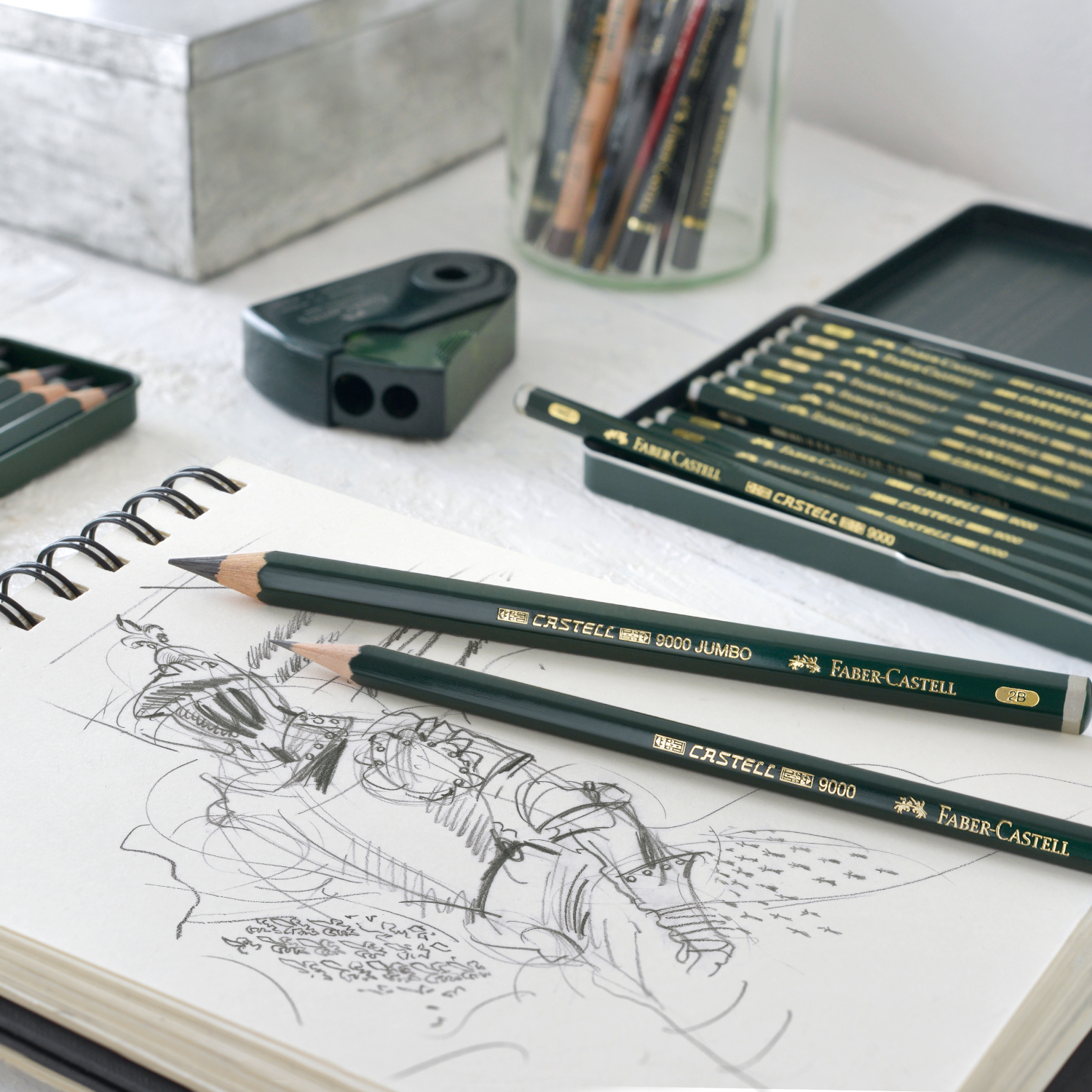 Bleistift Castell 9000 Jumbo auf Skizzenbuch, umgeben von Faber Castell Zubehör in elegantem Grün.