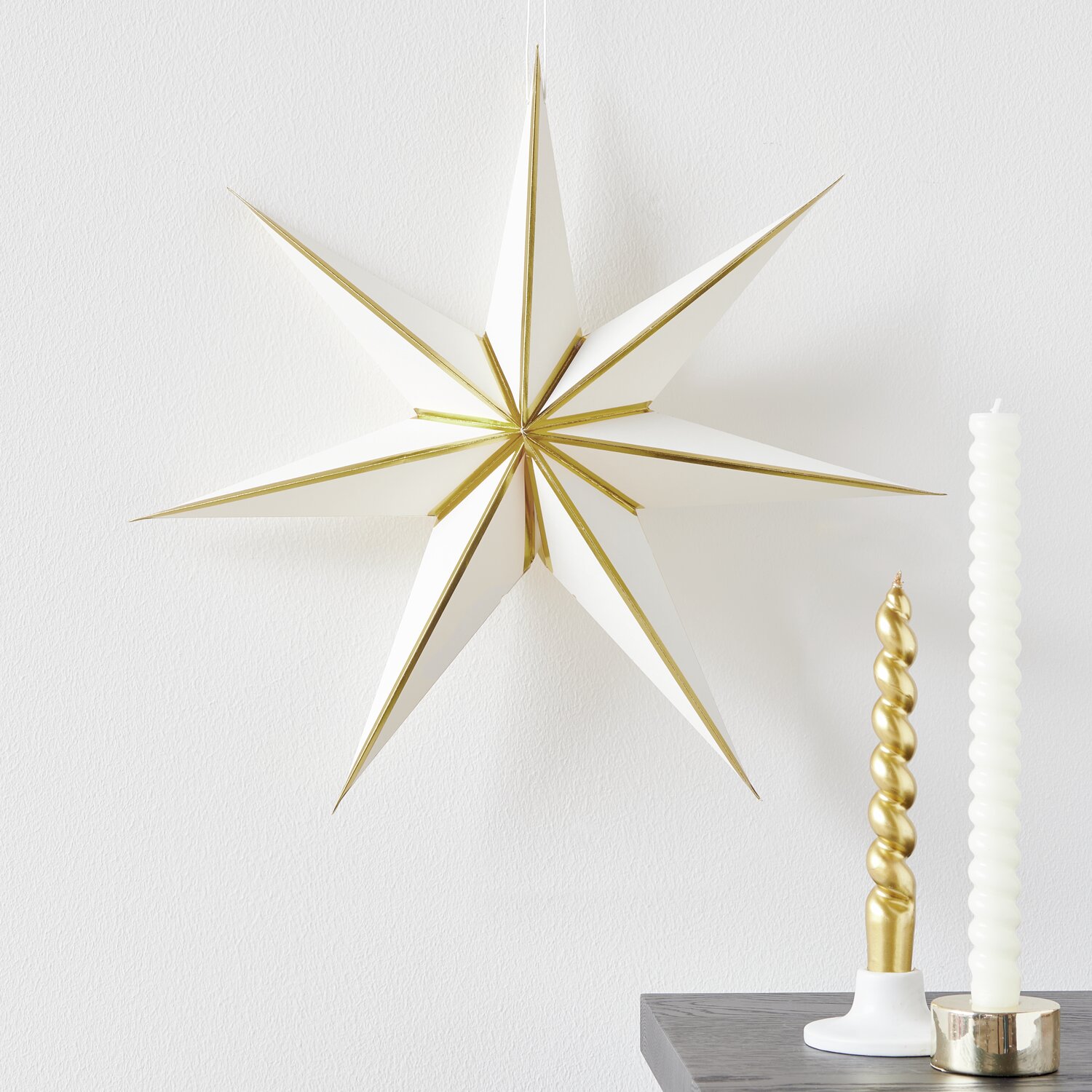 Papierstern in Weiß und Gold von Rico Design, Ø45cm, dekoriert neben Kerzen auf einem Tisch.