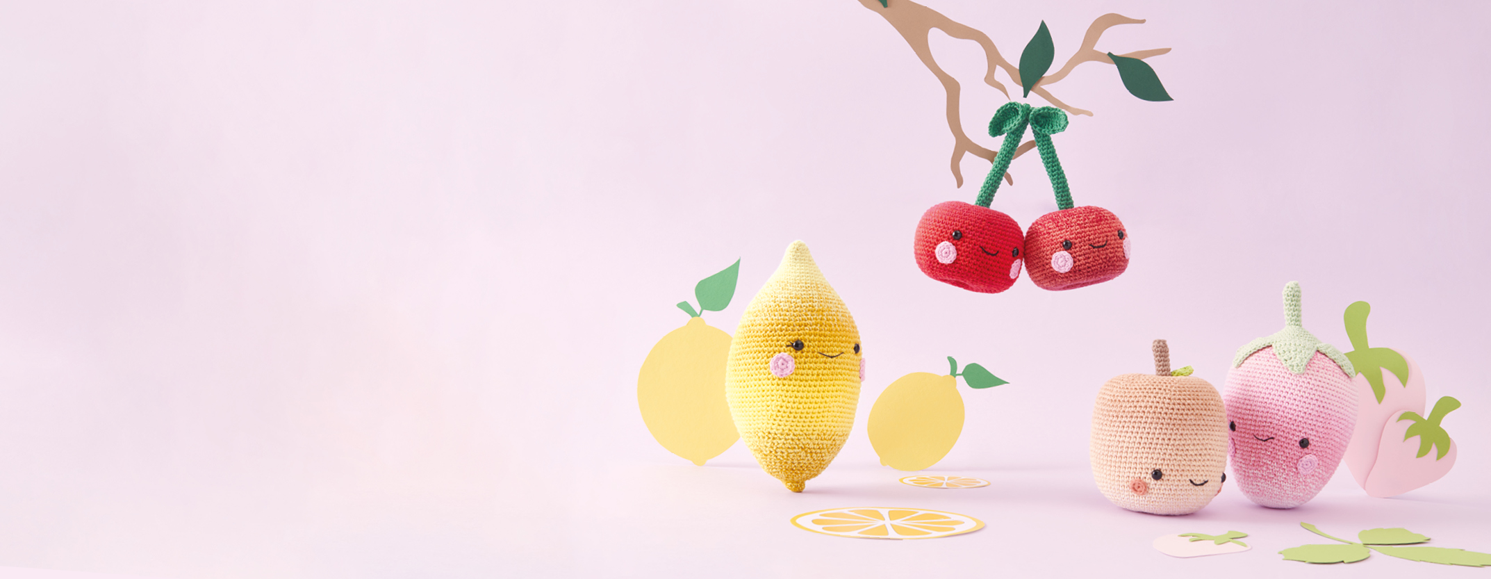 Gehäkelte Kirschen, eine gehäkelte Zitrone, ein gehäkelter Apfel und eine gehäkelte Erdbeere mit Gesicht.