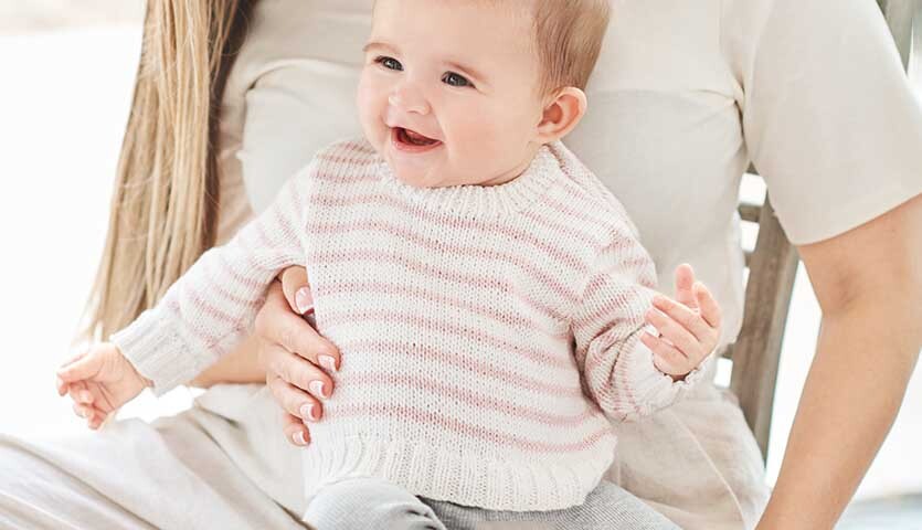 Strickanleitung Pullover aus Baby Organic Cotton Strickanleitung Pullover aus Baby Organic Cotton: Baby in gestreiftem Pullover auf dem Schoß einer Frau.