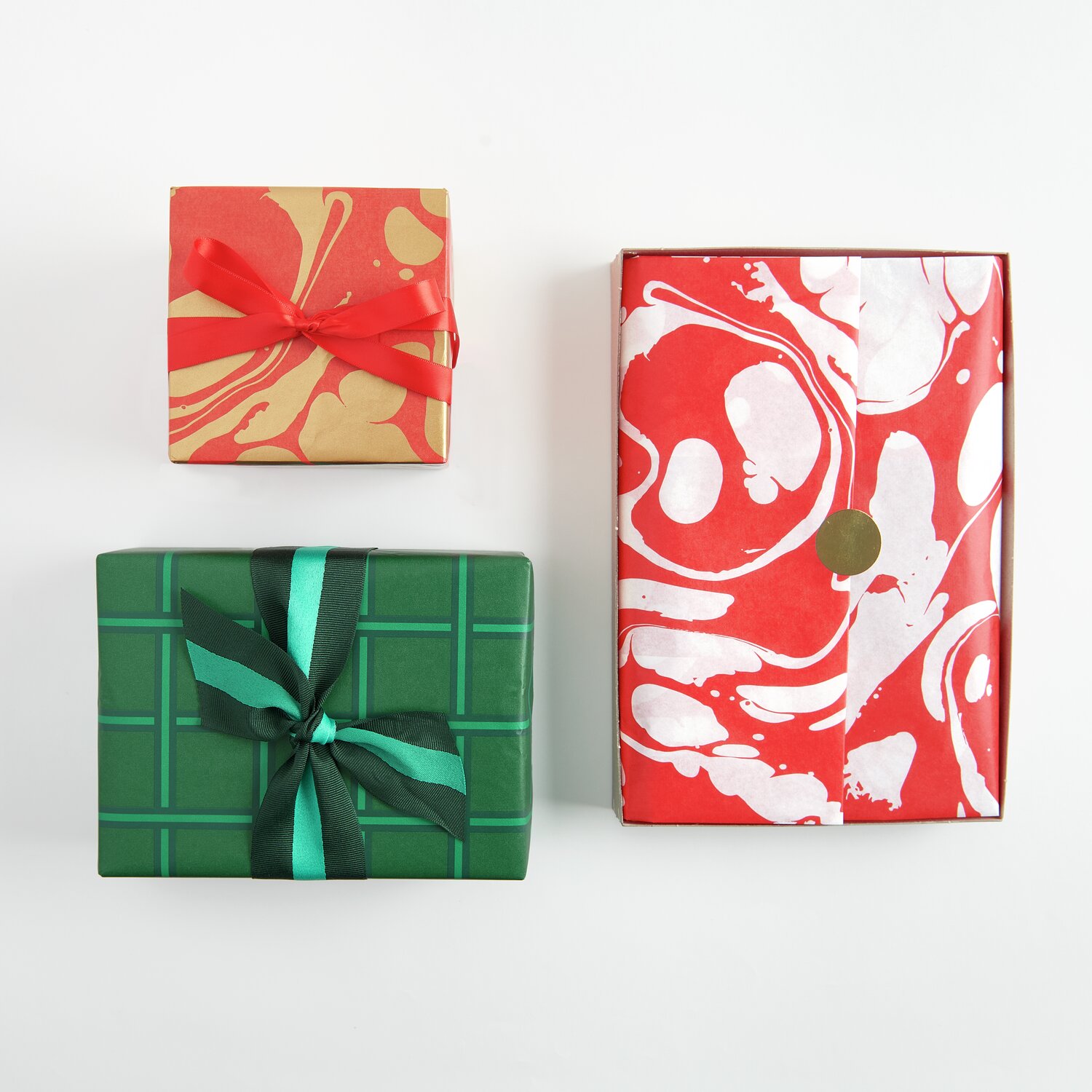 Seidenpapier Raster Grün 4m: Drei Geschenke in grünem, rotem und marmoriertem Papier, kunstvoll verpackt.