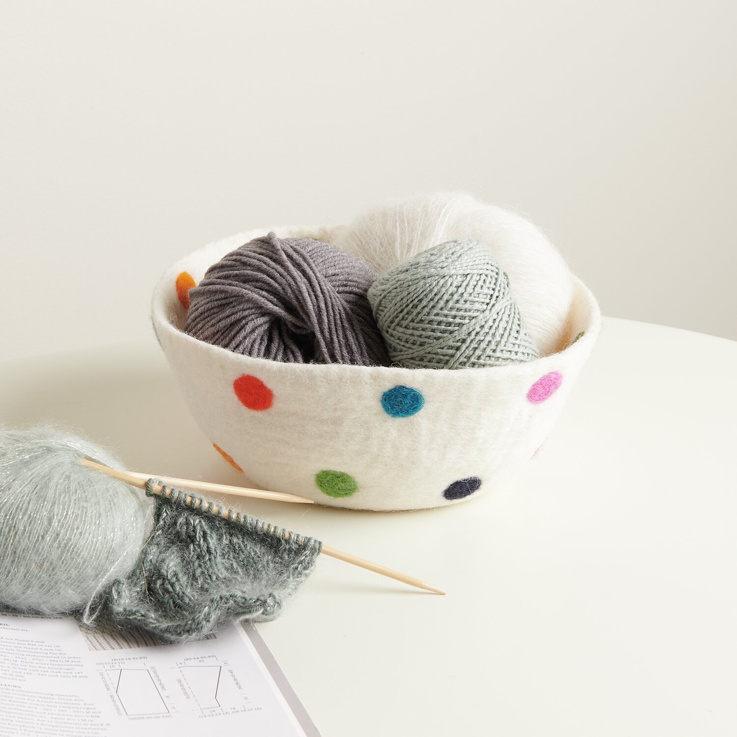 Filz-Korb bunt bepunktet handgefilzt, gefüllt mit bunten Wollknäueln auf einem Tisch.