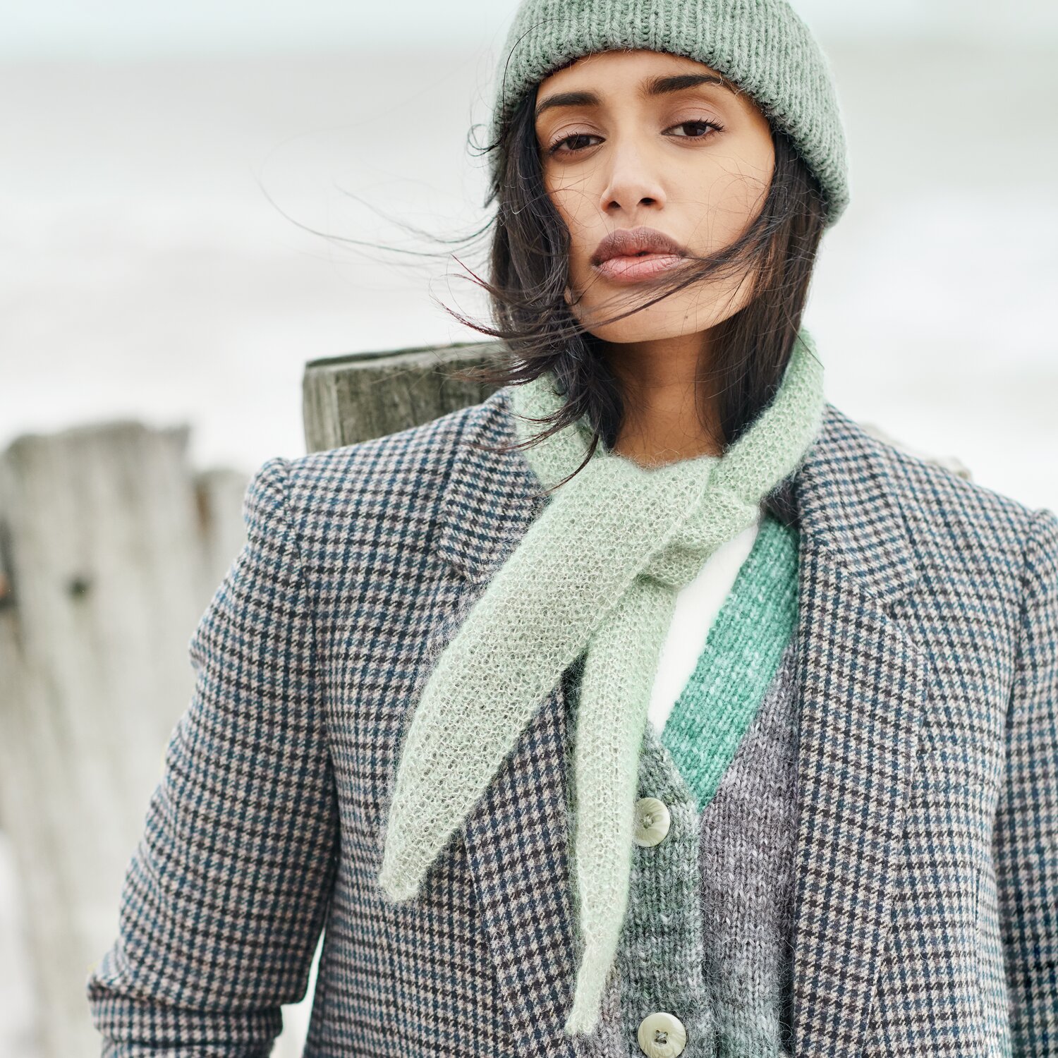 Strickset Minituch Modell 03 aus Lovewool No. 21 von Rico Design Strickset Minituch Modell 03: Frau mit mintgrünem Schal und Mütze, kariertem Mantel am Strand.
