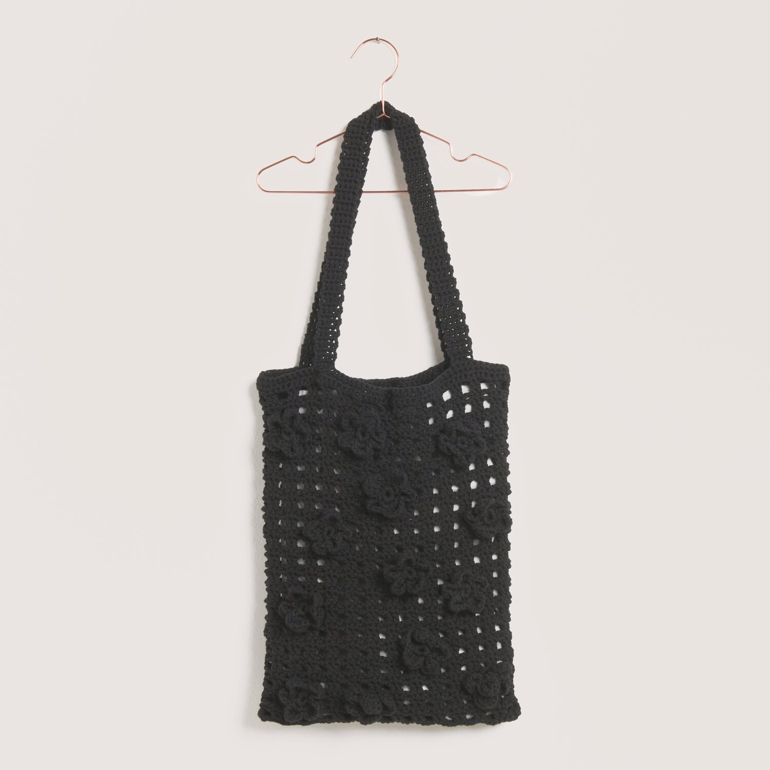 Made by Me No. 22 Frühjahr-Sommer: Schwarze gehäkelte Tasche mit Blumenmuster, hängend an einem Kleiderbügel.