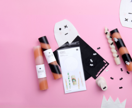 Halloween-Bastelset mit Kerzenfolien, Anleitung, schwarzen Servietten und Dekoelementen auf rosa Hintergrund.