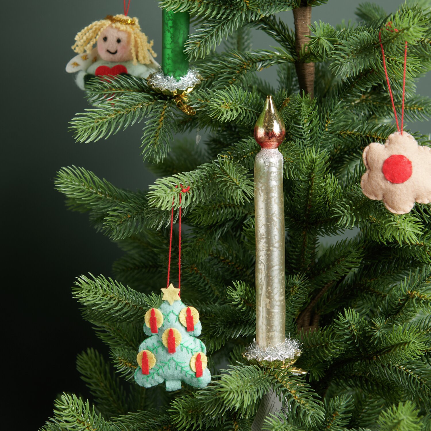 Baumschmuck Glaskerze mit goldenem Metallchip, umgeben von Filzanhängern an einem Tannenbaum.