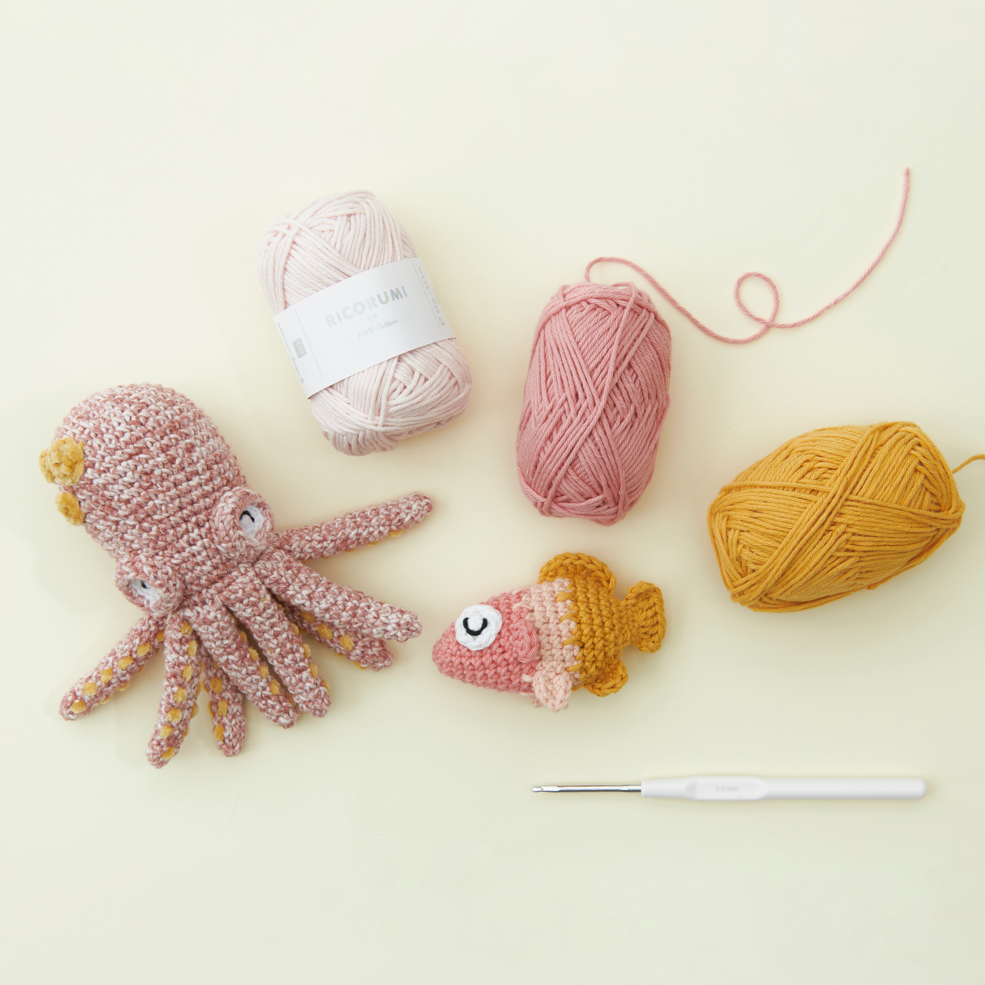 Eine gehäkelte Qualle und ein gehäkelter Fisch mit den zugehörigen Garnen und Häkelnadel. Flatlay von Produkten.