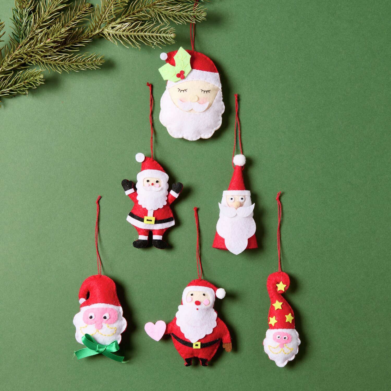 Aufhänger Filz-Santa mit Sternen Rot/Weiß: Sechs weihnachtliche Filzanhänger in Rot und Weiß auf grünem Hintergrund.