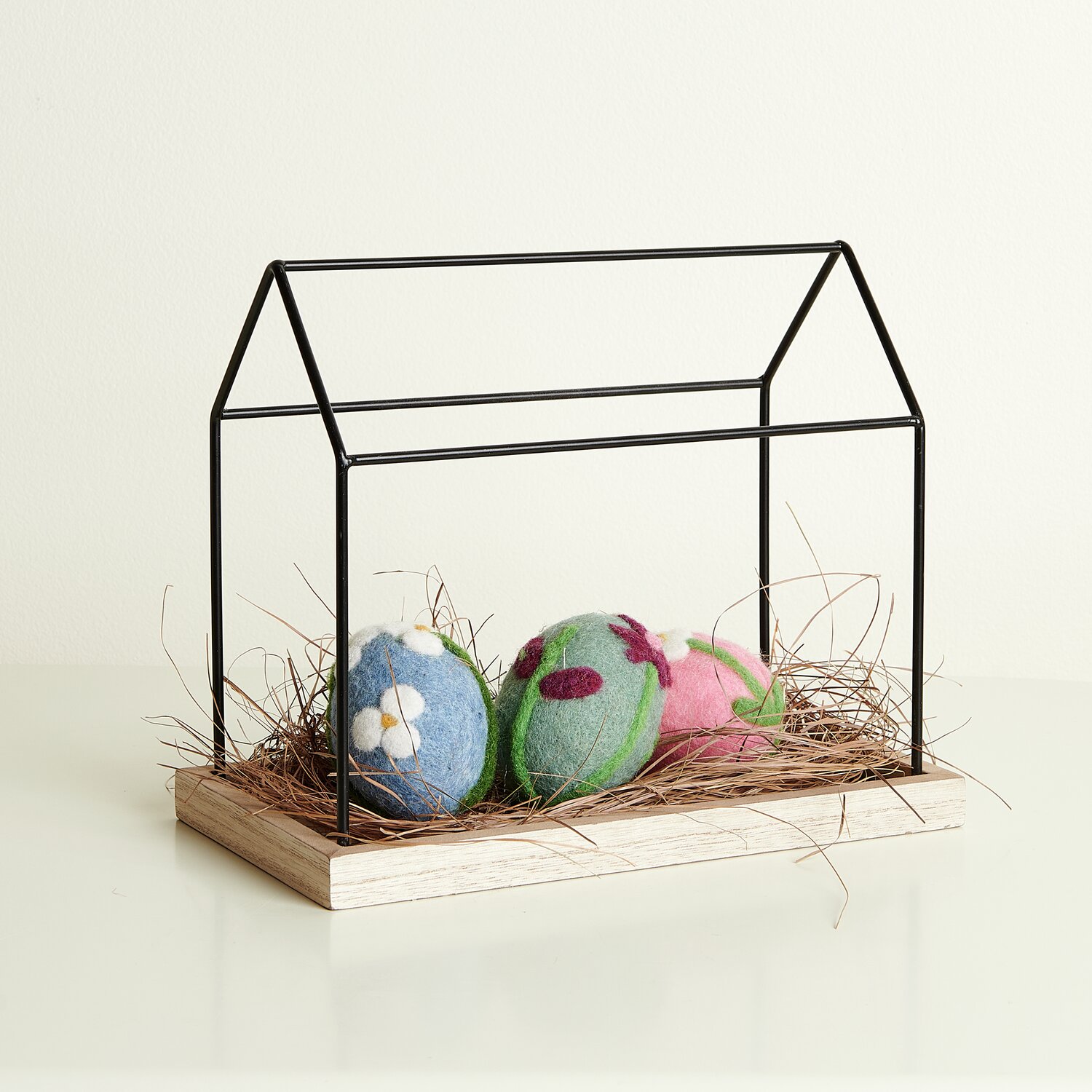 Metall Haus mit Holzboden: Schwarzes Metallgestell auf Holz, dekoriert mit bunten Filzkugeln.