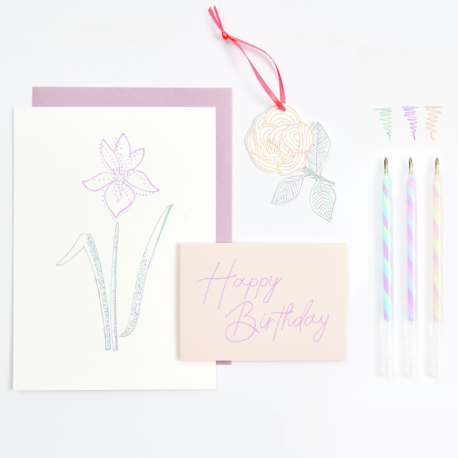 Gelstift Neon-Twist: Drei bunte Gelstifte neben einer Geburtstagskarte mit Blumenmotiv und Anhänger.