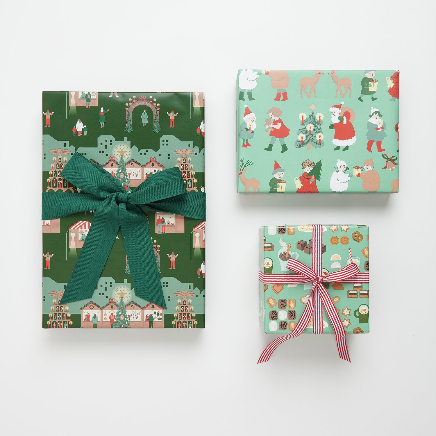 Paper Poetry Geschenkpapier Weihnachtsmarkt Mix: Drei Geschenke mit festlichen Motiven, verziert mit grünen und rot-weißen Bändern.