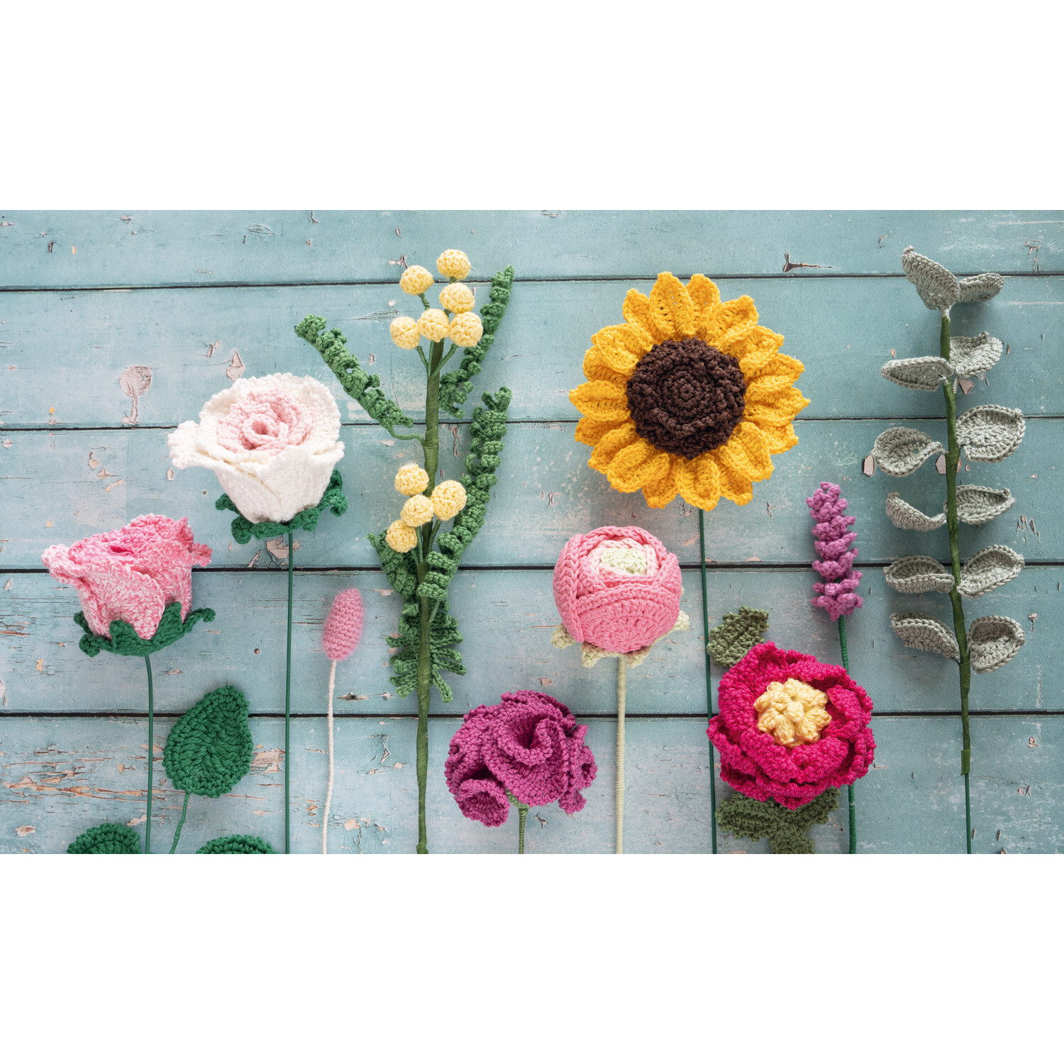 Mein bunter Häkelgarten - 100 wunderschöne Blumen und Blüten: Bunte Häkelblumen auf blauem Holz.