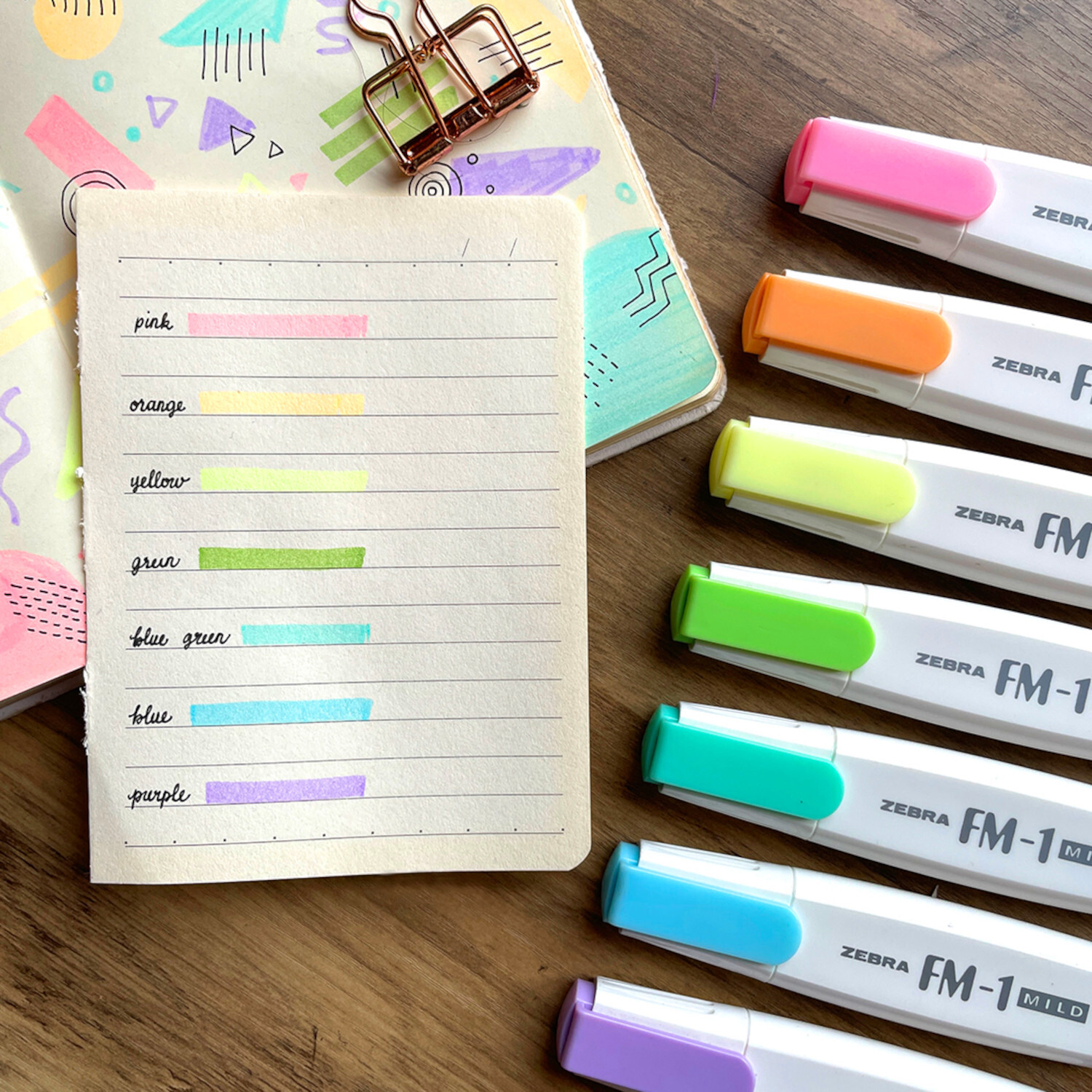 Textmarker FM-1 mild: Sechs bunte ZEBRA-Textmarker neben einem Notizbuch mit Farbmuster.