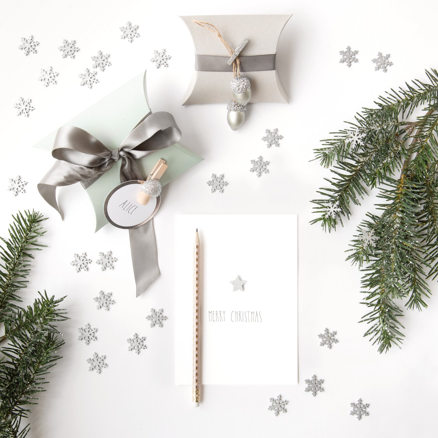 Holzklammern mit Glitter 4x30mm 24 Stück, umgeben von Tannenzweigen und silbernen Schneeflocken.