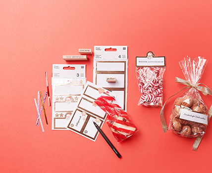 Drei verschiedenen Kekstüten mit Keksen, Nüssen und Bonbons gefüllt, daneben weihnachtliche Papieretiketten, Stempel und Verschlüsse. Flatlay von Produkten. 