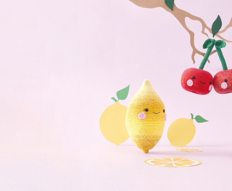 Gehäkelte Kirschen, eine gehäkelte Zitrone, ein gehäkelter Apfel und eine gehäkelte Erdbeere mit Gesicht.