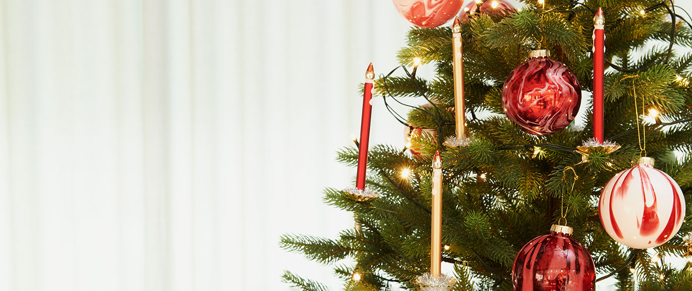 Ein Tannenbaum mit unterschiedlichen roten Christbaumkugeln und Glaskerzen. Fotosetting weißer Hintergrund und Tannenbaum.