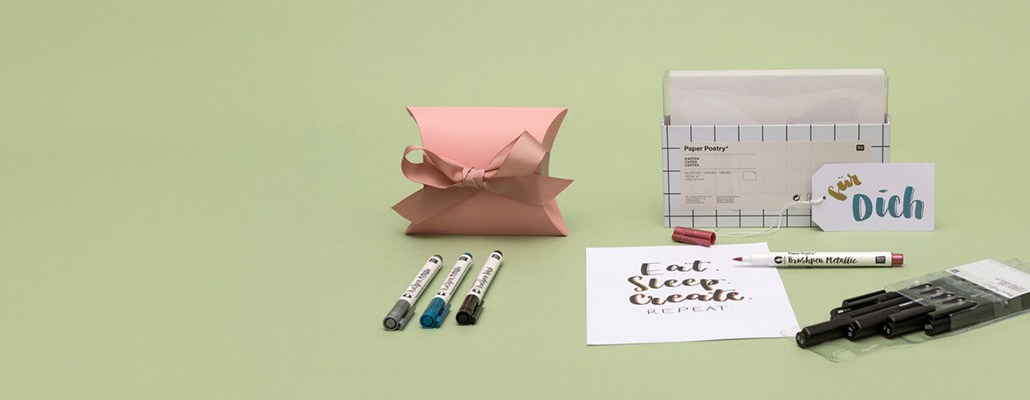 Weiße Karten in der Verpackung, eine Geschenkschachtel, eine beschriftete Karte und Geschenkanhänger mit Brushpens und verpackten Pigment Linern.