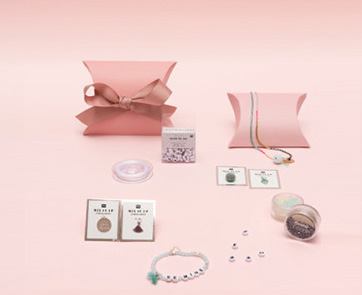 Geschenkschachteln mit Schmuckperlen, -band und -anhänger. Mehrere pinke Geschenkschachteln mit Schmuckperlen, Schmuckband und verschiedenen Anhängern. Fotosetting rosa Wand.