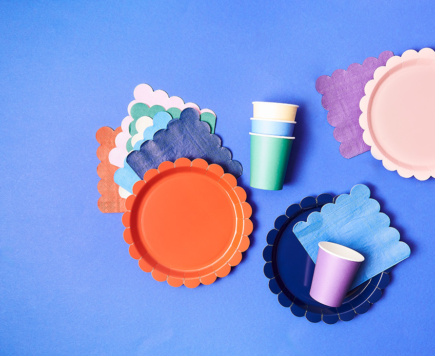 Zusammenpassende Papierteller, -becher und Servietten in verschiedenen Farben. Flatlay von Produkten.
