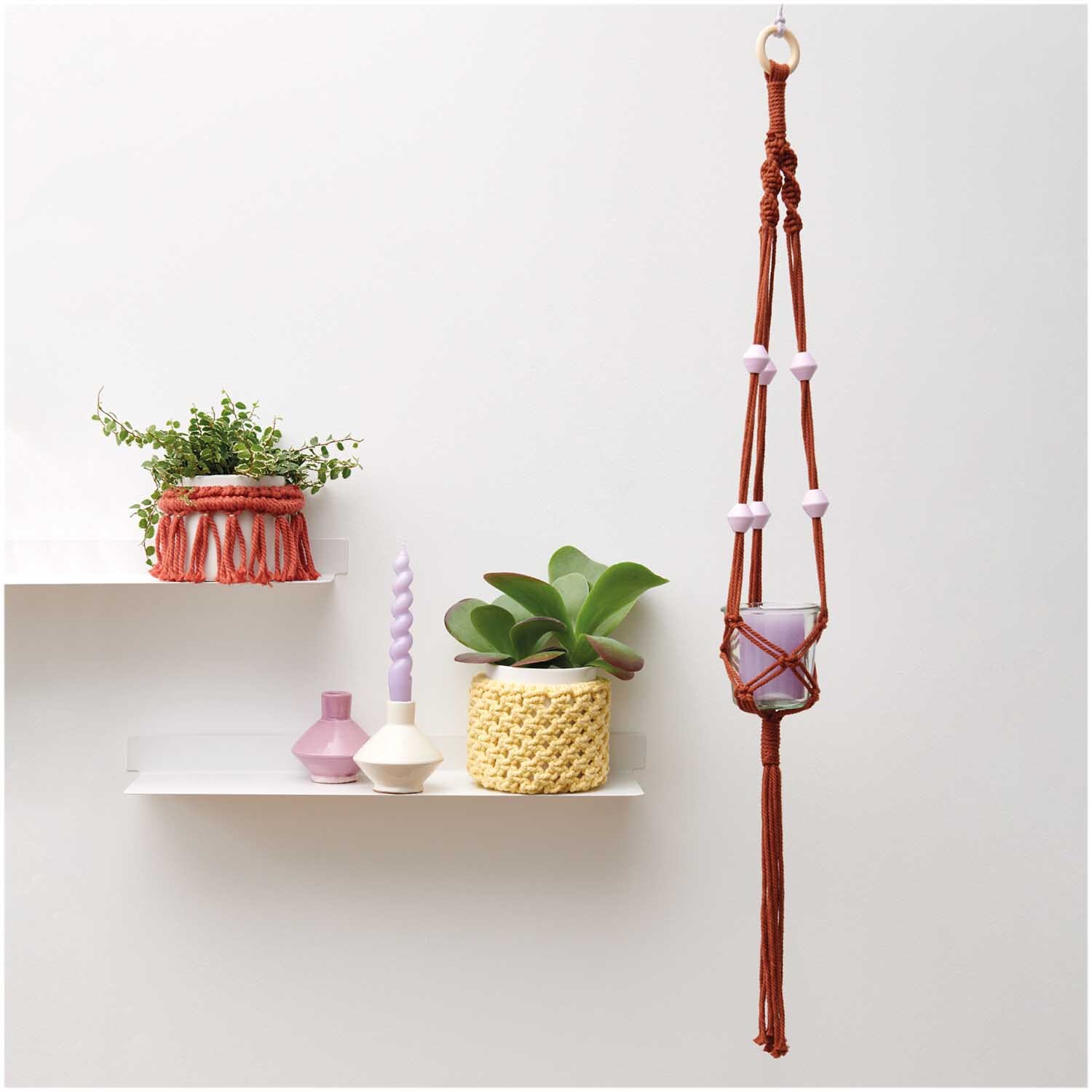 Creative Cotton Cord Makramee-Garn von Rico Design in einem Pflanzenhänger, dekoriert mit Pflanzen und Kerzen auf einem Regal.
