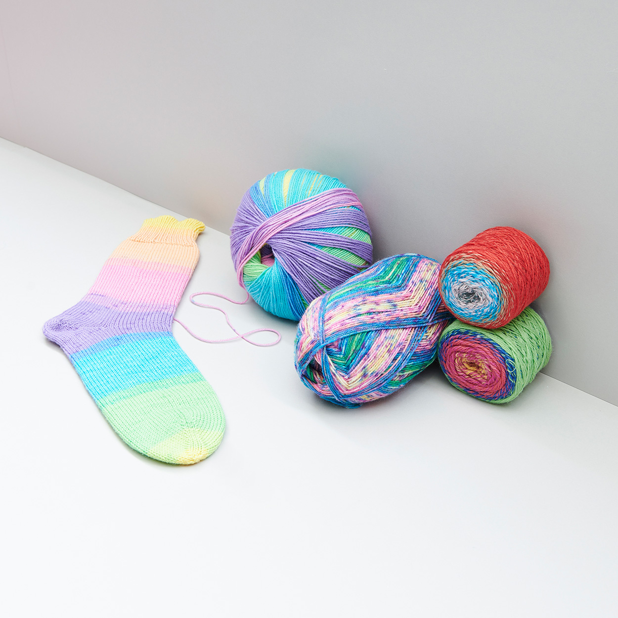 Bunte Garne mit einer bunten gestrickten Socke. Fotosetting graue Ecke.