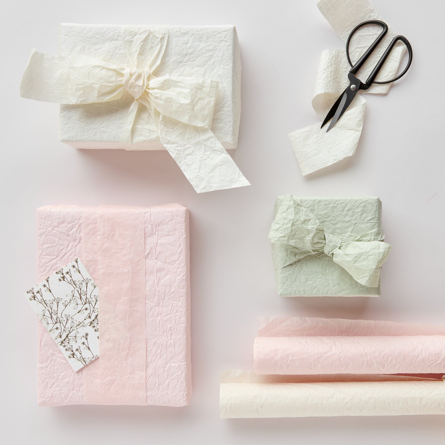 Knitter Geschenkpapier Mix Elfenbein/Apricot/Schilf zeigt dekorativ verpackte Geschenke mit passenden Knitter Papierbändern von Rico Design sowie Schere und Karte.