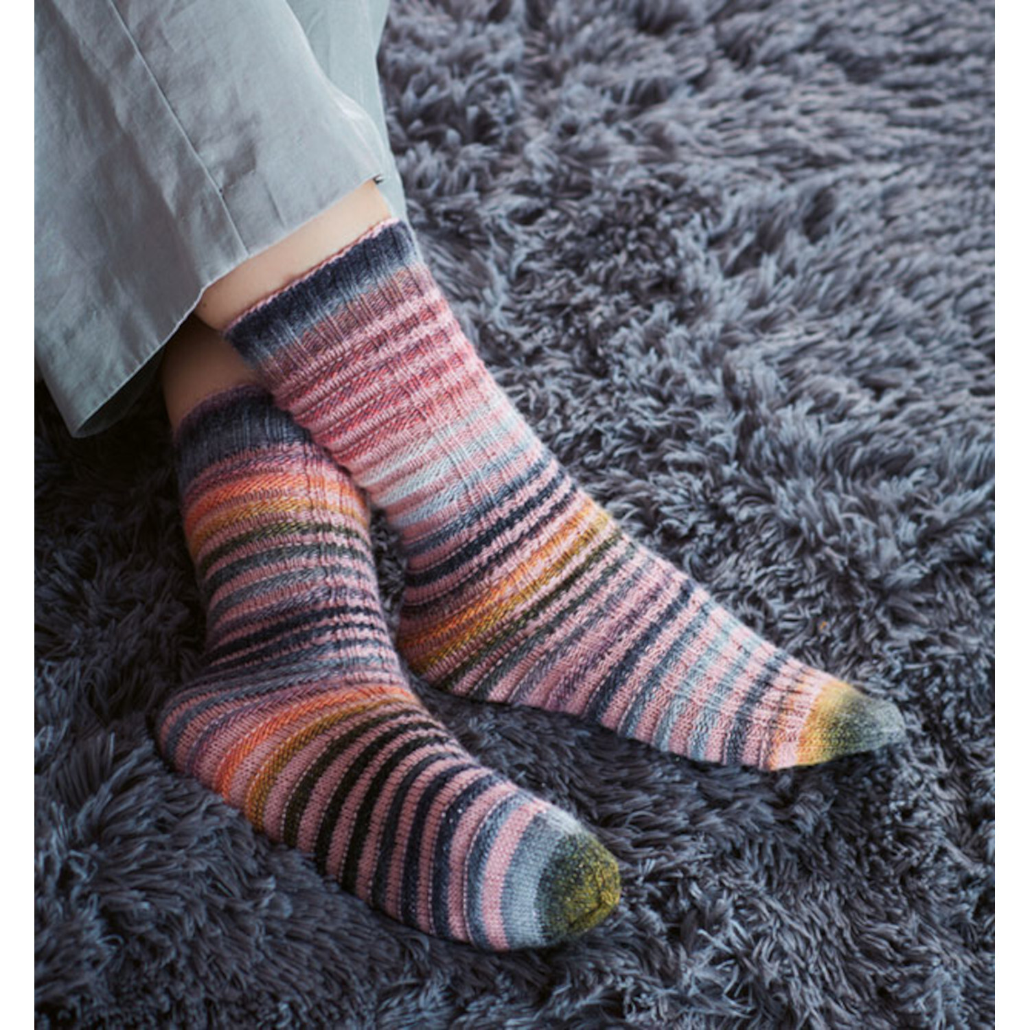 Tube Socks stricken: Bunte, gestreifte Socken auf grauem Teppich. Perfekt für gemütliche Tage.