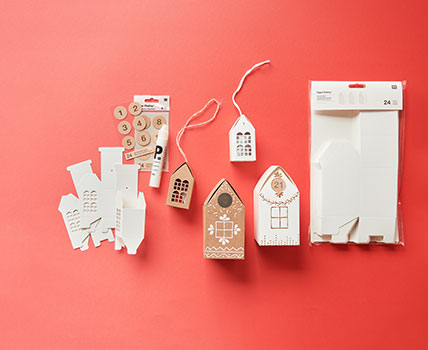 Geschenkschachteln in Häuserform mit Zahlenstickern und Farbe verziert. Flatlay von Produkten.