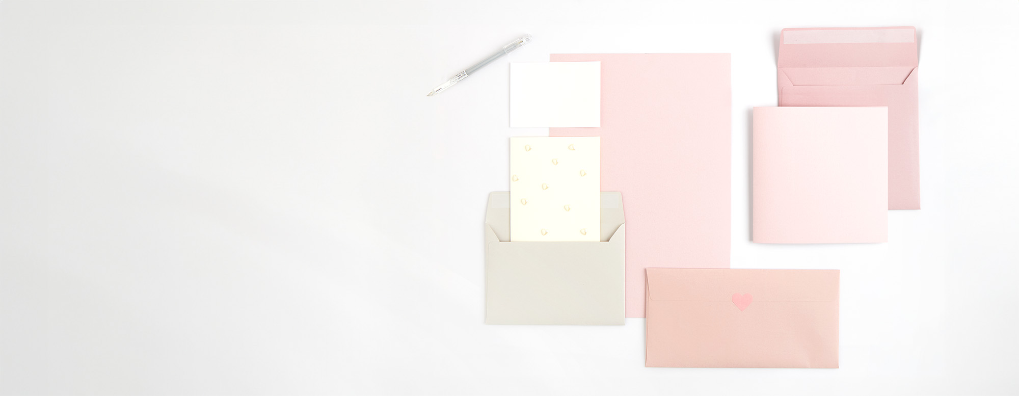 Rosa Papier darauf grauer Umschlag mit weißen Karten, sowie zwei rosa Umschläge mit heller Karte. Flatlay von Produkten.