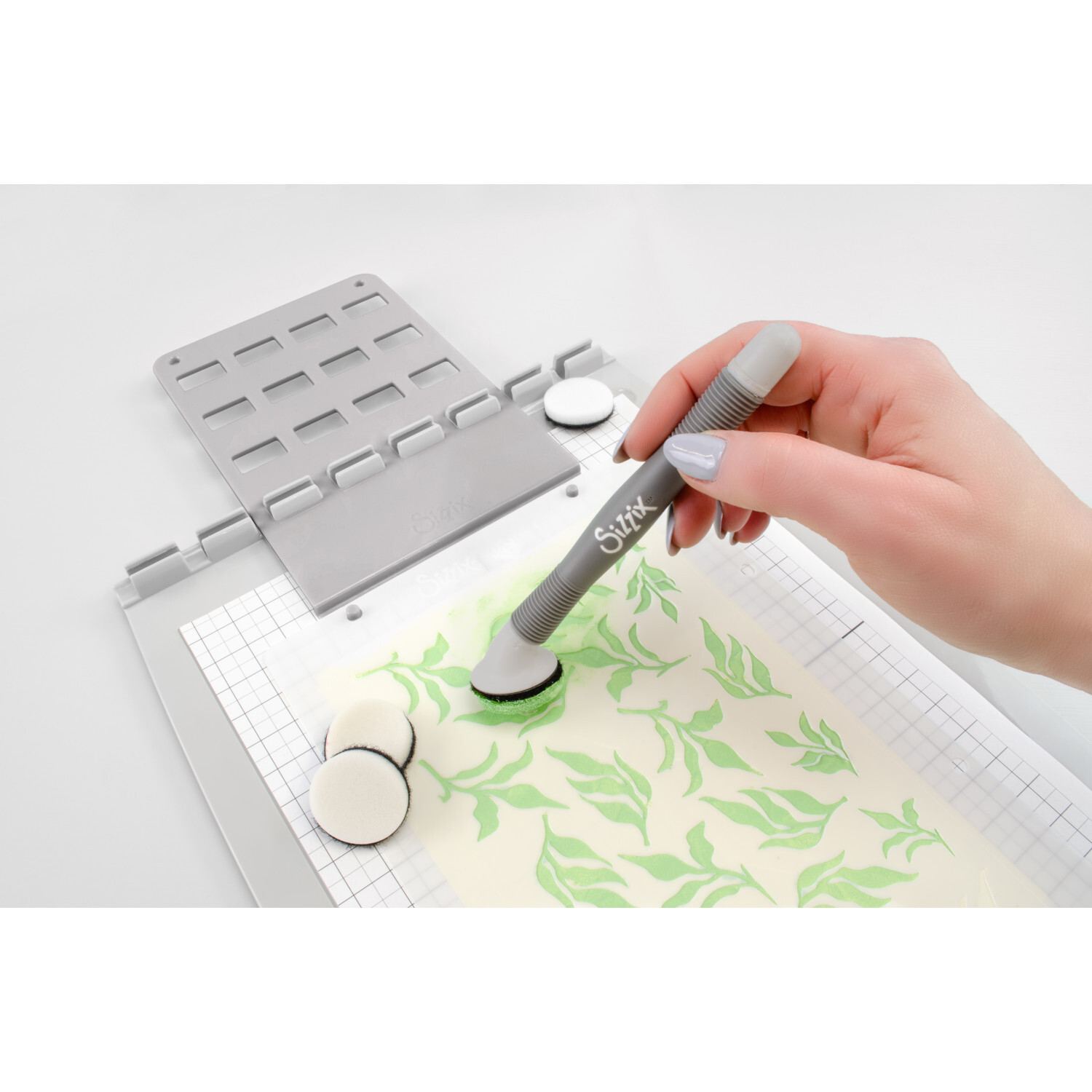 Studio Blending Tool Set Grey von idee. Creativmarkt Studio Blending Tool Set Grey: Hand nutzt graues Sizzix-Werkzeug zum Schablonieren auf Papier.