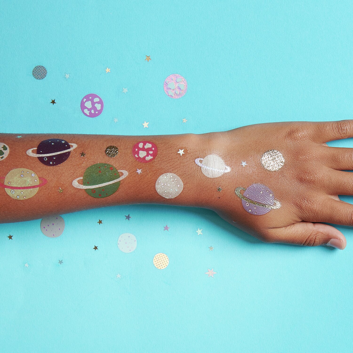 Tattoos Universum: 63-teiliges Set mit bunten Planeten-Tattoos auf einem Arm, vor blauem Hintergrund.