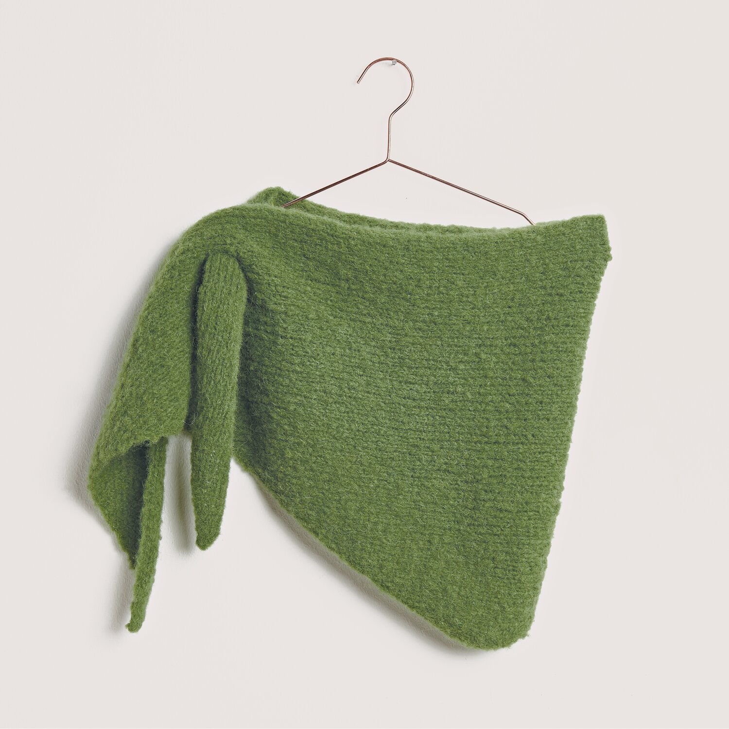 Luxury Pure Baby Alpaca 50g 150m Farbe Oliv von Rico Design Strickset Dreieckstuch Modell 12 aus Made by Me No. 21, olivgrün, aus Baby Alpaca, hängt an einem Kleiderbügel.