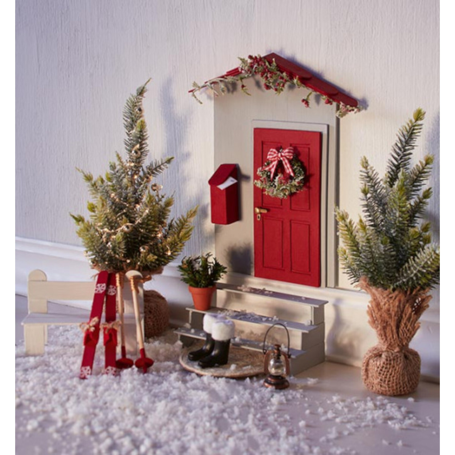 Weihnachtliche Wichteltüren: Rote Tür mit Kranz, umgeben von Tannen und Dekoration im Schnee.