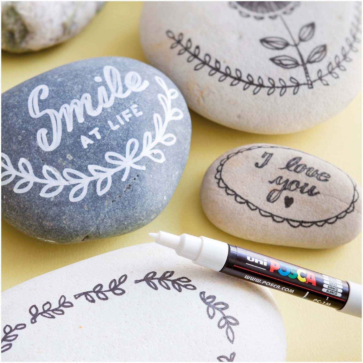 POSCA-Marker PC-3M verziert Steine mit kunstvollen Mustern und Schriftzügen in verschiedenen Farben.