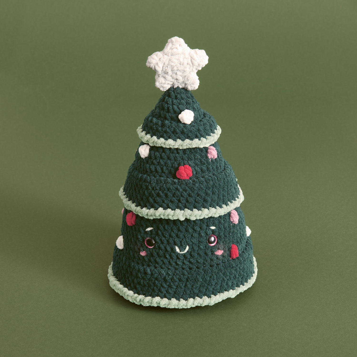 Ein kleiner gehäkelter Weihnachtsbaum mit Gesicht. Fotosetting grüner Hintergrund.