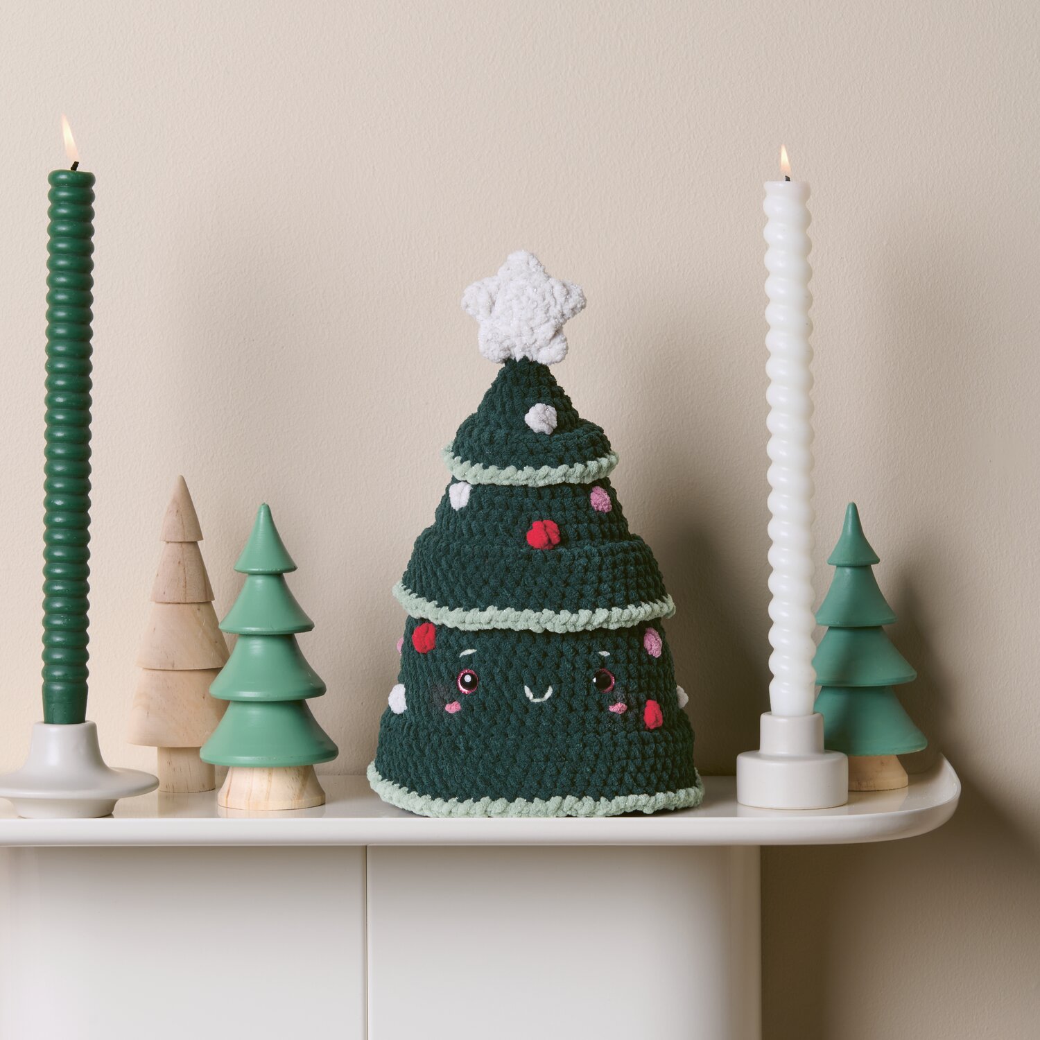Häkelset Weihnachtsbaum Modell 4 aus Chenillove Sparkle Christmas: Grüner Baum mit Dekoration auf weißem Tisch, umgeben von Kerzen und kleinen Bäumen.