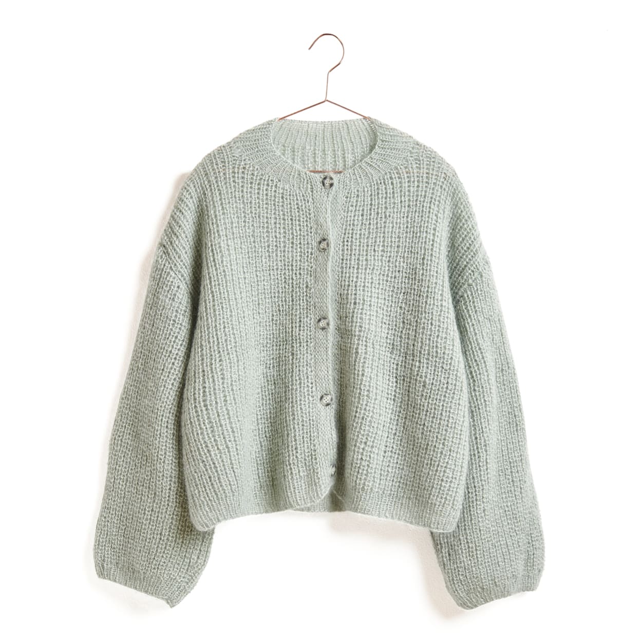 Eine Strickjacke in Salbeigrün hängt an einem Kleiderbügel.