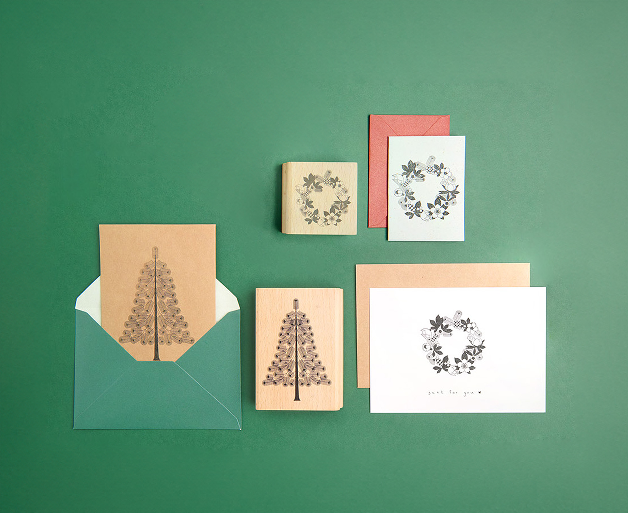 Karten mit Umschlägen in verschiedenen Farben und Größen mitgestempelten Weihnachtsbäumen und Blumenkranz. Flatlay von Produkten.