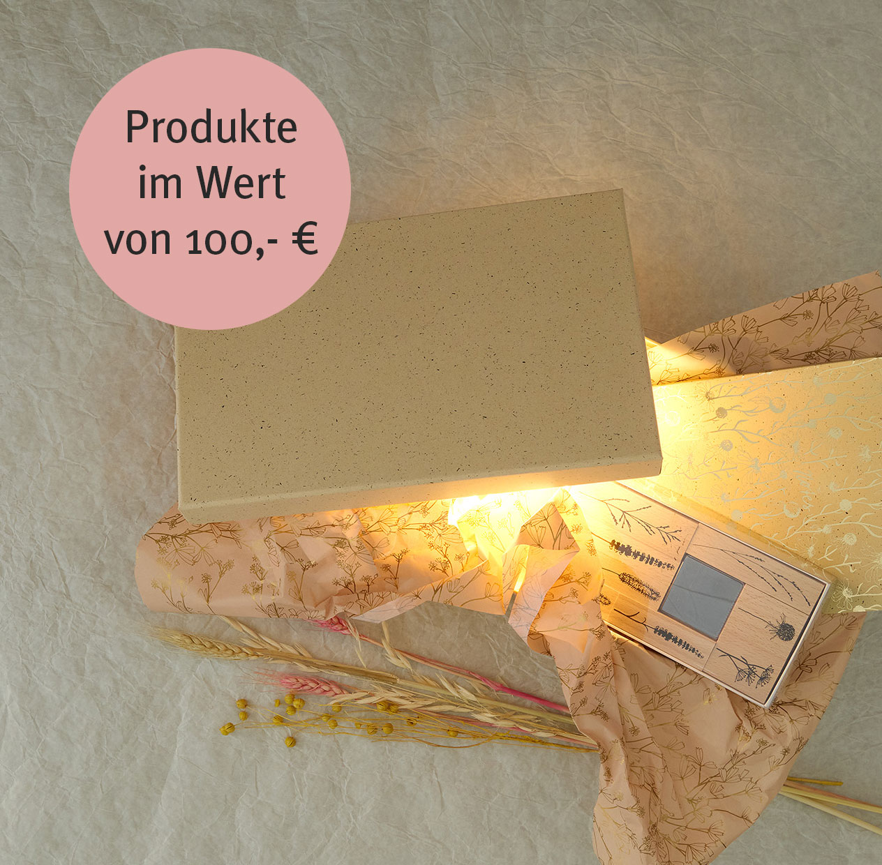 Beleuchtete Geschenkbox mit Seidenpapier, Trockenblumen und kleiner Grußkarte auf hellem Hintergrund.