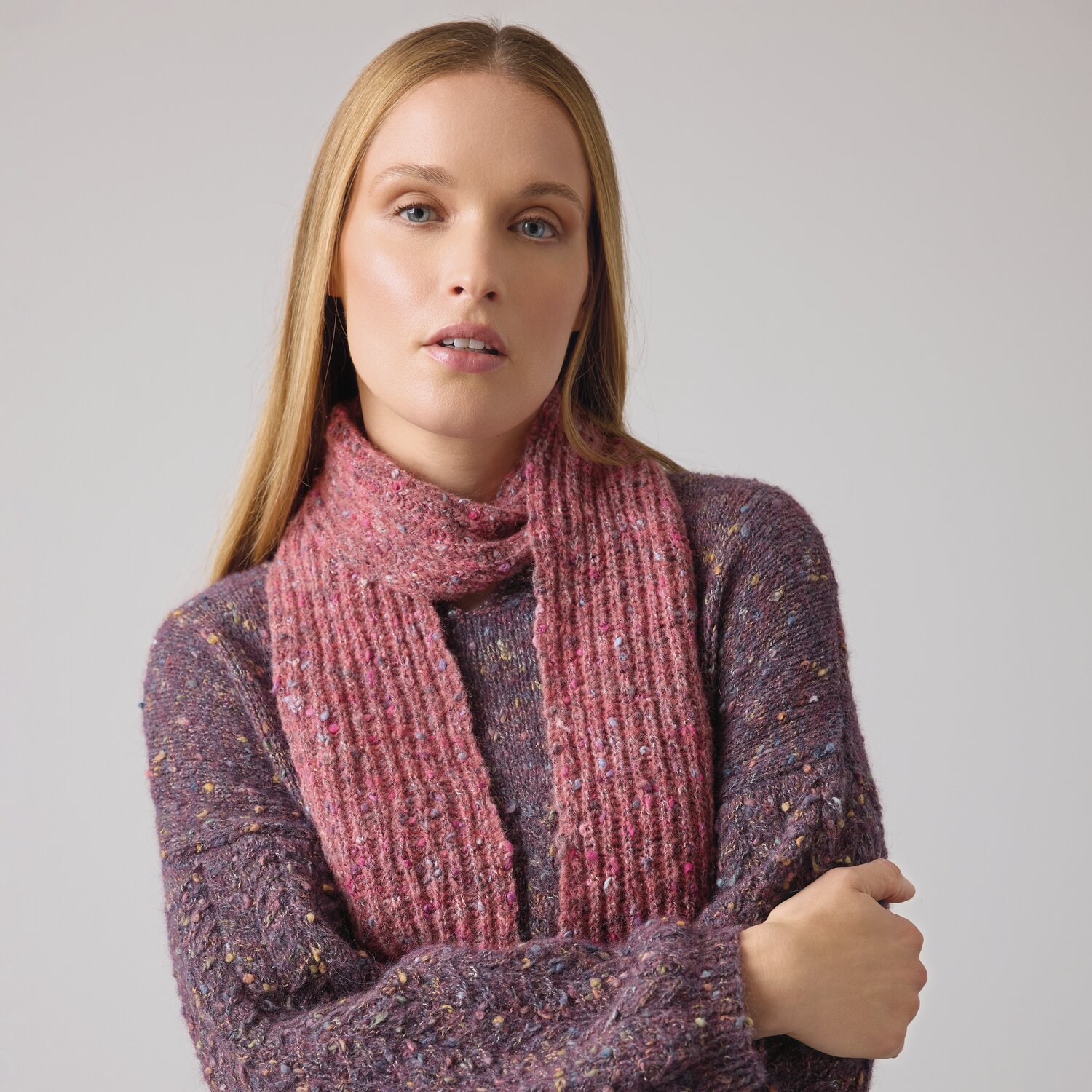 Strickset Schal Modell 09 aus Die Neue Masche No. 14 von idee. Creativmarkt Strickset Schal Modell 09 aus DNM 14: Frau trägt rosa Schal und lila Pullover, stilvoll und modern.