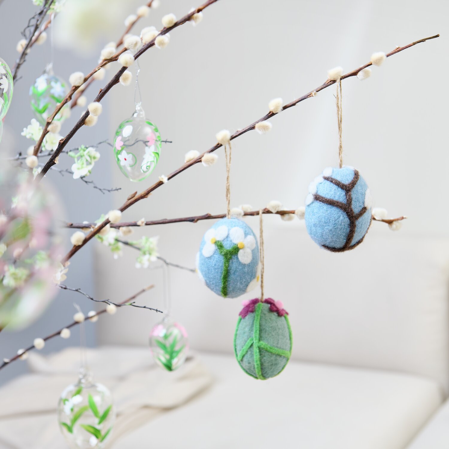 Aufhänger Filz-Ei Kirschblüte: Filz-Eier in Blau und Grün mit floralen Mustern an einem dekorativen Zweig.