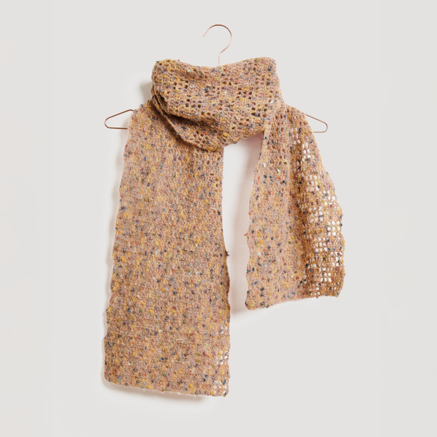 Lovewool No. 21 Herbst-Winter Sprachauswahl deutsch von Rico Design Ein gestrickter Schal in warmen Erdtönen hängt auf einem Kleiderbügel. Der Schal ist von der Marke Modell Legeware und zeichnet sich durch ein offenes, luftiges Strickmuster aus.