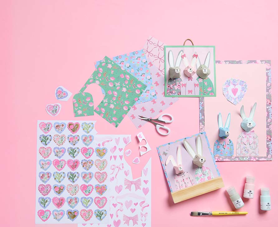 Gebastelte Osterhasen und Bastelpapier in verschiedenen Farben und Mustern und Acrylfarben mit Pinsel. Flatlay von Produkten.