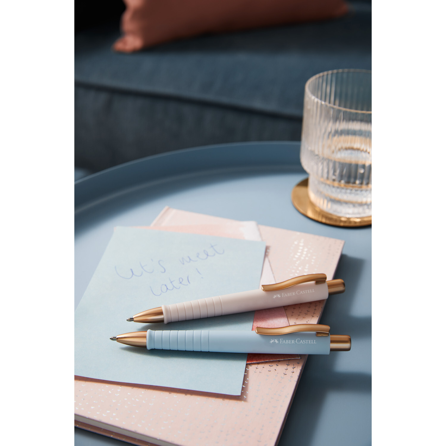 Kugelschreiber Poly Ball Urban XB Farbe Stone Grey von Faber-Castell Kugelschreiber Poly Ball Urban XB auf blauem Tisch mit Notizbuch und Glas, Faber Castell.