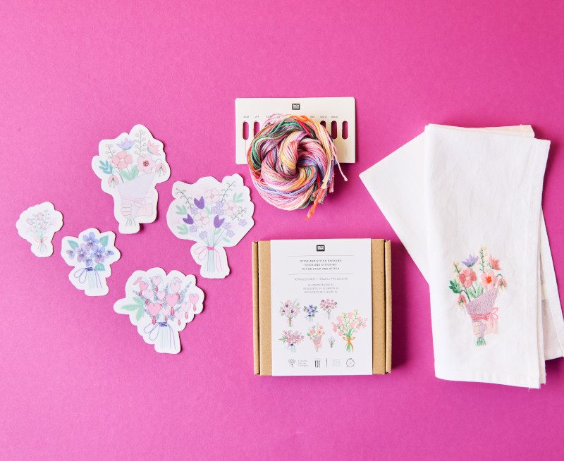 Ein Stick and Stitch Set aus der Kollektion The Sky Is The Limit mit floralen Motiven, daneben ein bereits bestickter Stoff. Flatlay von Produkten.