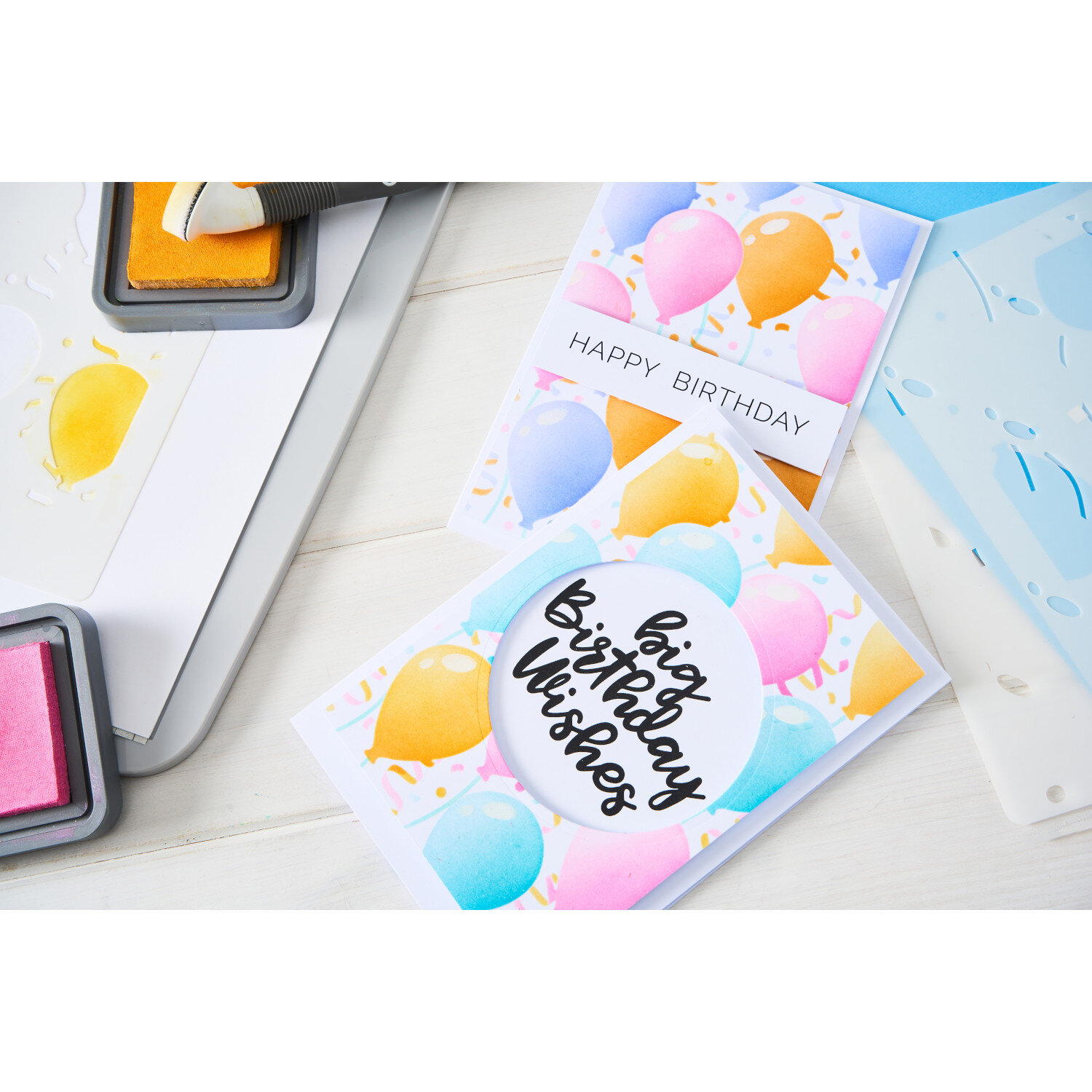 Sizzix Layered Stencils Birthday Balloons 4 PK A6 zeigt bunte Luftballon-Geburtstagskarten im A6-Format mit Tintenpads und Schablonen auf hellem Basteltisch