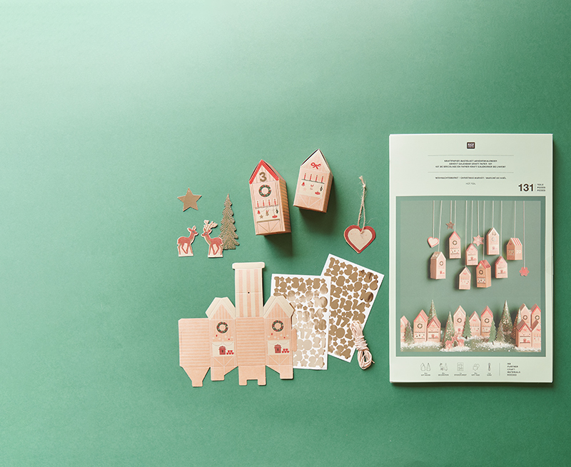 Adventskalender Bastelset mit Papphäusern und Zahlenstickern. Ein Adventskalender Bastelset mit Schachteln in Hausform und Zahlen-Stickern. Flatlay von Produkten.