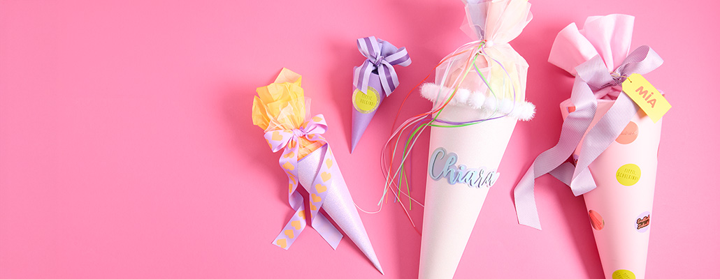 Rosa- und lilafarbene Schultüten in unterschiedlichen Größen und Designs. Flatlay von Produkten.
