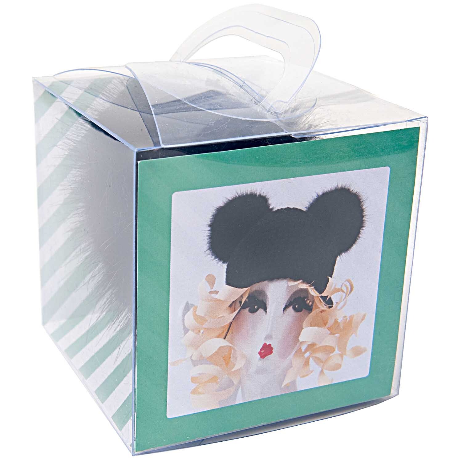 Kunstfellbommel 10cm von Rico Design in einer transparenten Box mit stilvollem Design und grünem Hintergrund.